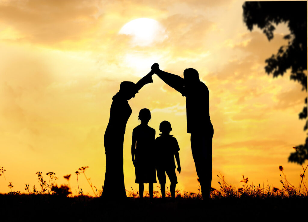 Silhouettes de deux parents formant un toit protecteur au-dessus de deux enfants au coucher du soleil